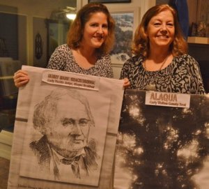 BRENDA REES (right) and daughter Lauren Rees display images of Henry Marie Brackenridge and live oak trees on his Alaqua property. The anniversary of Walton County's founding was celebrated on Dec. 29, as has been the tradition since 2004. Brenda Rees, initiator of the event, hosted the celebration at her Eastern Lake home. (Photo by Dotty Nist)